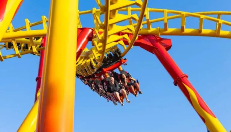 Imagem mostra uma montanha russa com pessoas curtindo uma volta em um dia de céu bem azul.