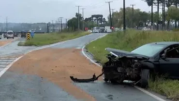 Imagem mostra um carro preto acidentado em uma curva com serragem no asfalto.