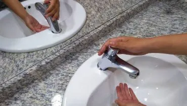Imagem mostra uma pessoa tentando lavar a mão em uma torneira sem água.