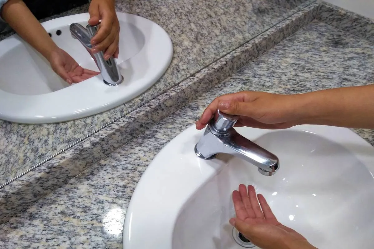 Imagem mostra uma pessoa tentando lavar a mão em uma torneira sem água.