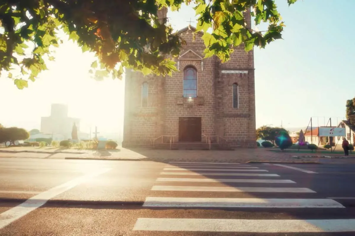 Imagem mostra uma igreja com raios de sol passando por uma árvore num dia muito frio.