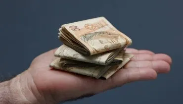 Imagem mostra um close de uma mão com varias notas de R$ 50 dobradas.