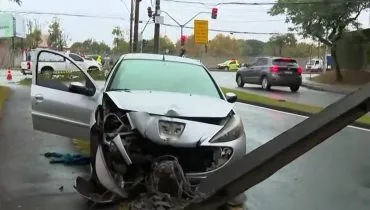 Imagem mostra um carro prata acidentado em Curitiba. O veículo está com a frente destruída e atrás de poste derrubado.