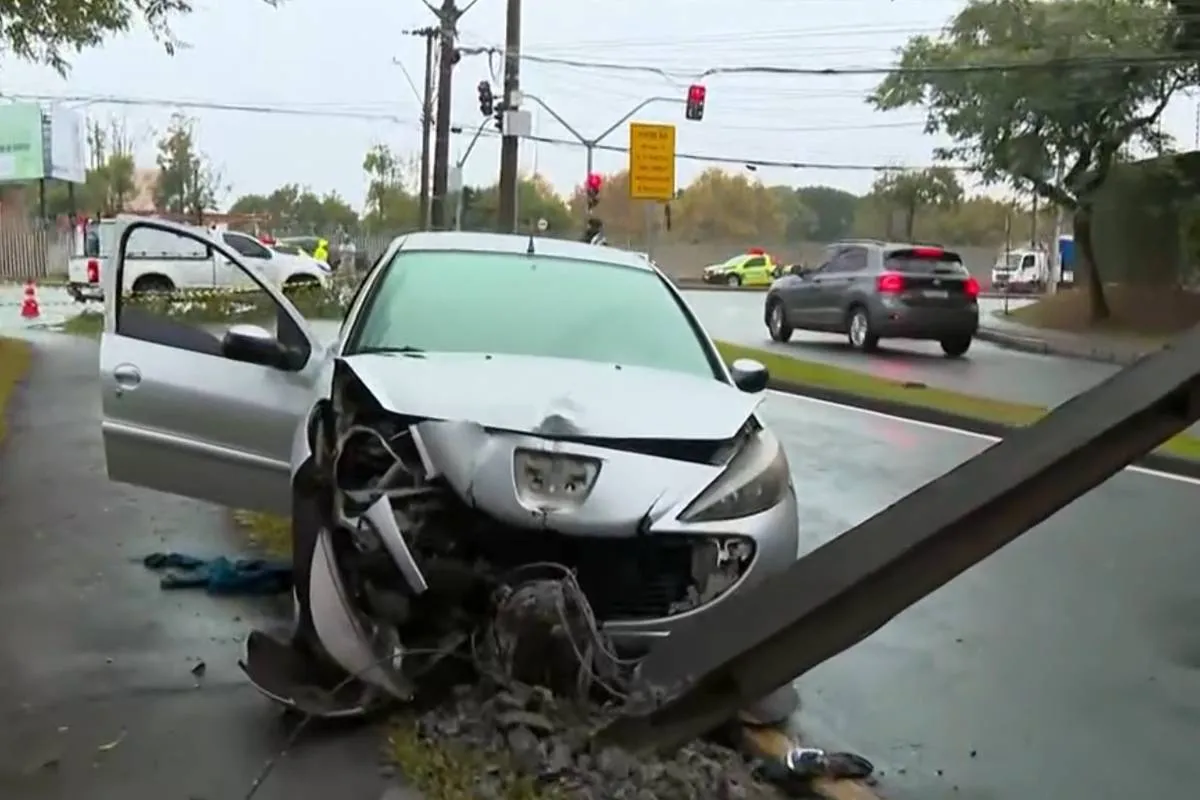 Imagem mostra um carro prata acidentado em Curitiba. O veículo está com a frente destruída e atrás de poste derrubado.