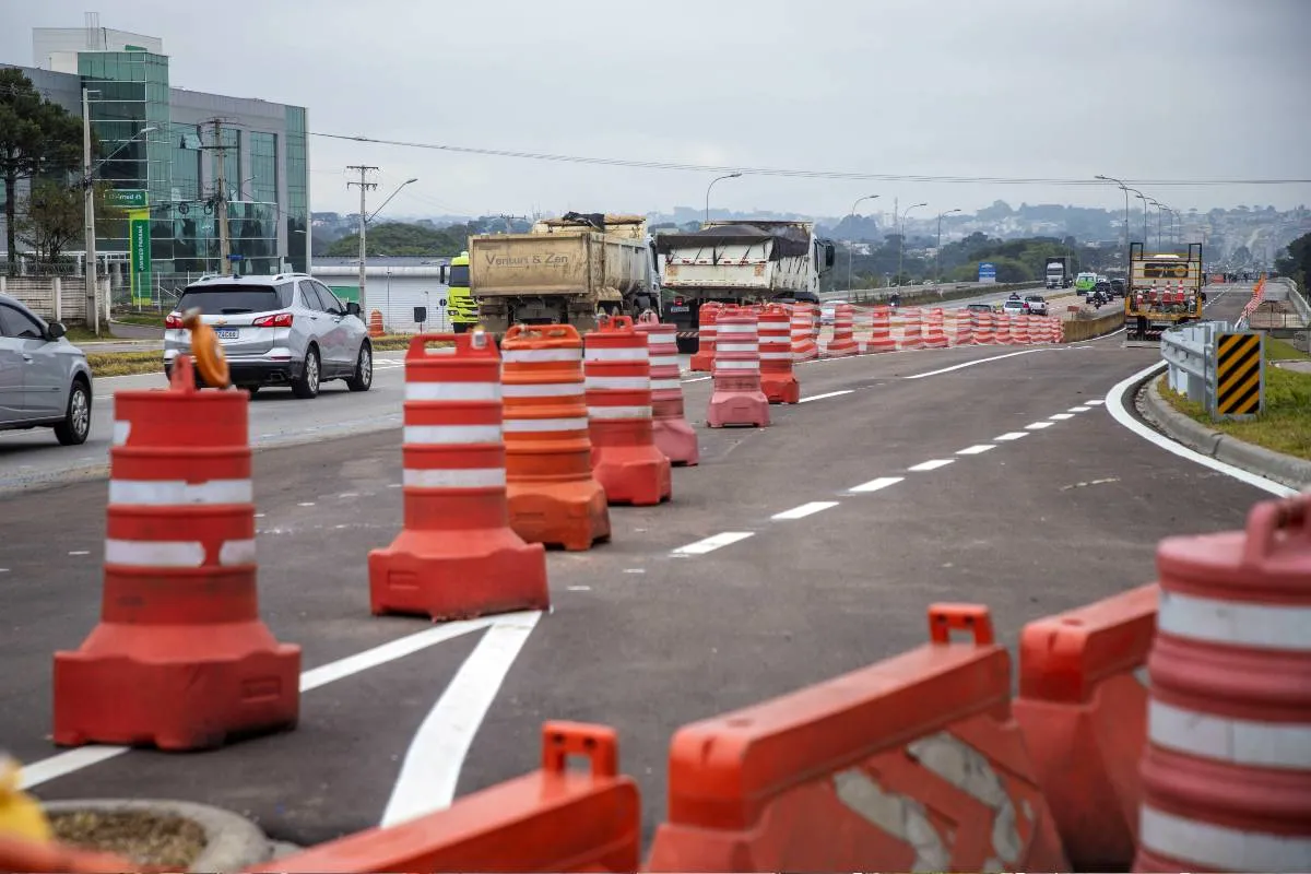 Imagem mostra cones de trânsito em um trecho da Linha Verde, em um dia nublado e com caminhões e carros circulando ao fundo.