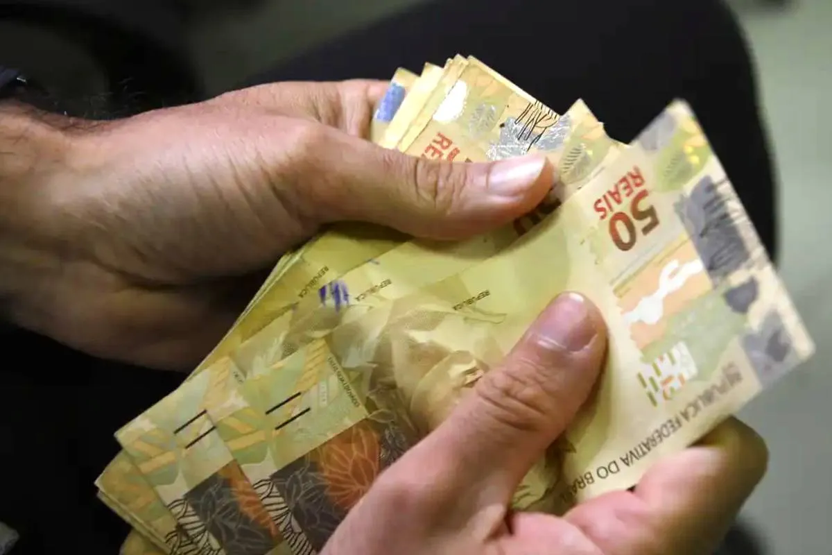 Imagem mostra uma pessoa segurando um leque de notas de R$ 50.