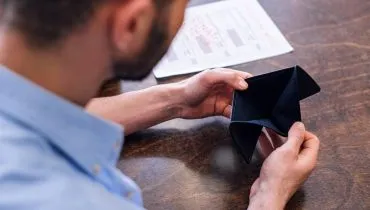 Imagem mostra um homem de camisa azul segurando uma carteira vazia.
