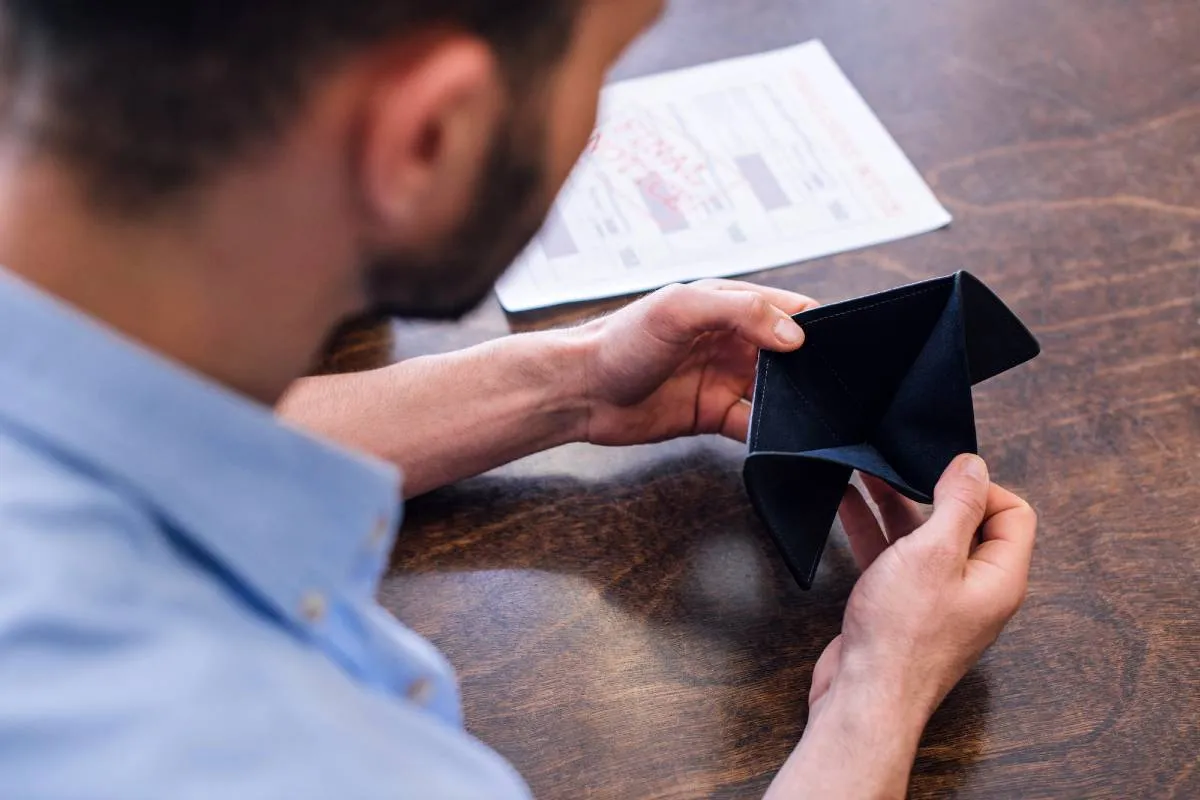 Imagem mostra um homem de camisa azul segurando uma carteira vazia.