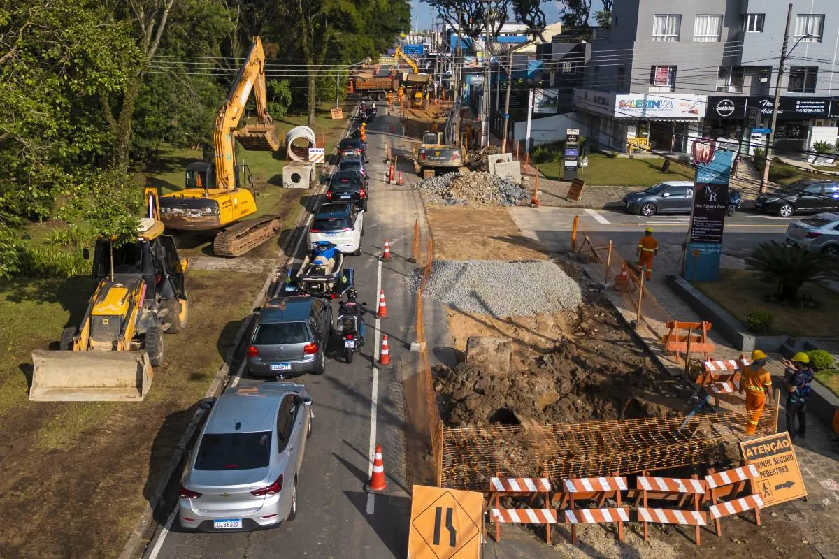 Imagem aérea mostra uma obra em andamento em um bairro de Curitiba, com máquinas, bloqueios e cones na pista.