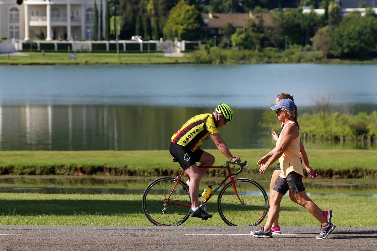 Imagem mostra um ciclista e pessoas caminhando em um parque de Curitiba, o Barigui.