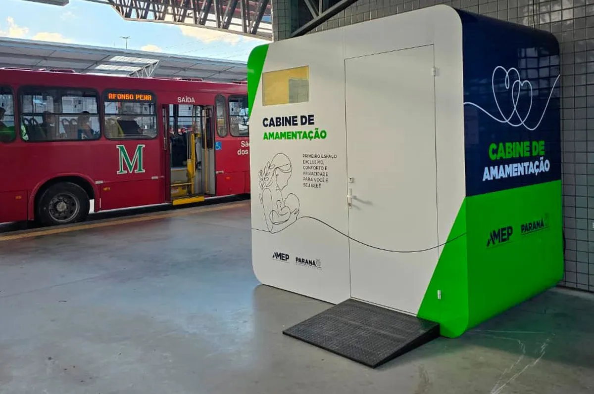 Imagem mostra um ônibus parado dentro do terminal de São José ao fundo. No primeiro plano, uma grande caixa com porta chamada cabine de amamentação