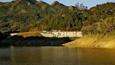 Imagem mostra parte da represa do Capivari, no nível da água, com a BR-116 ao fundo, com caminhão passando pela estrada