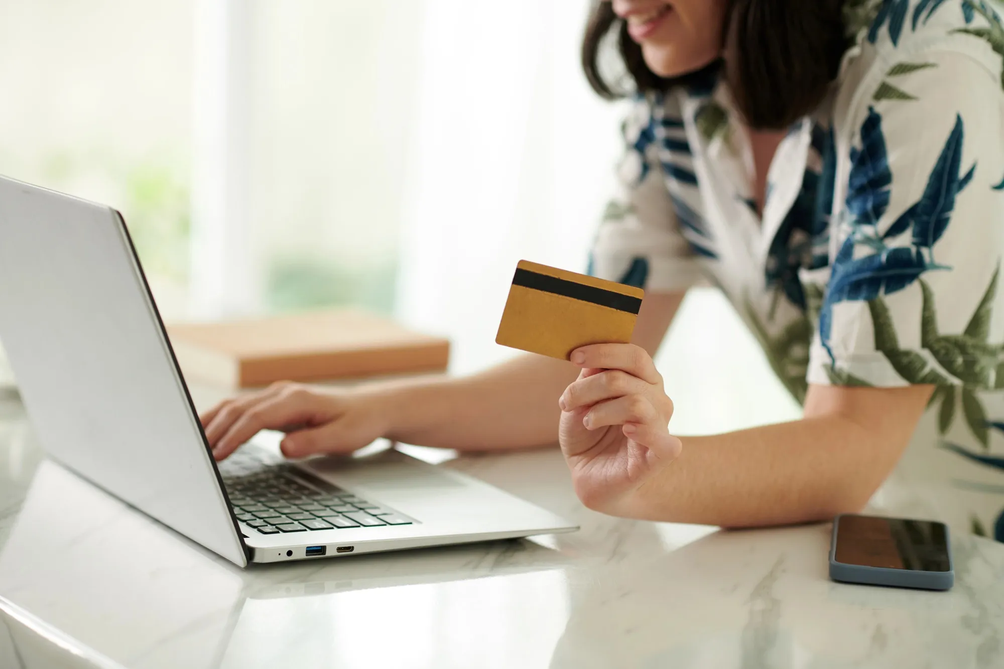imagem mostra mulher com cartão de crédito fazendo compra pelo notebook