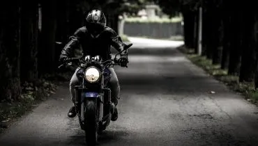 Imagem com um motociclista dirigindo numa rua vazia.