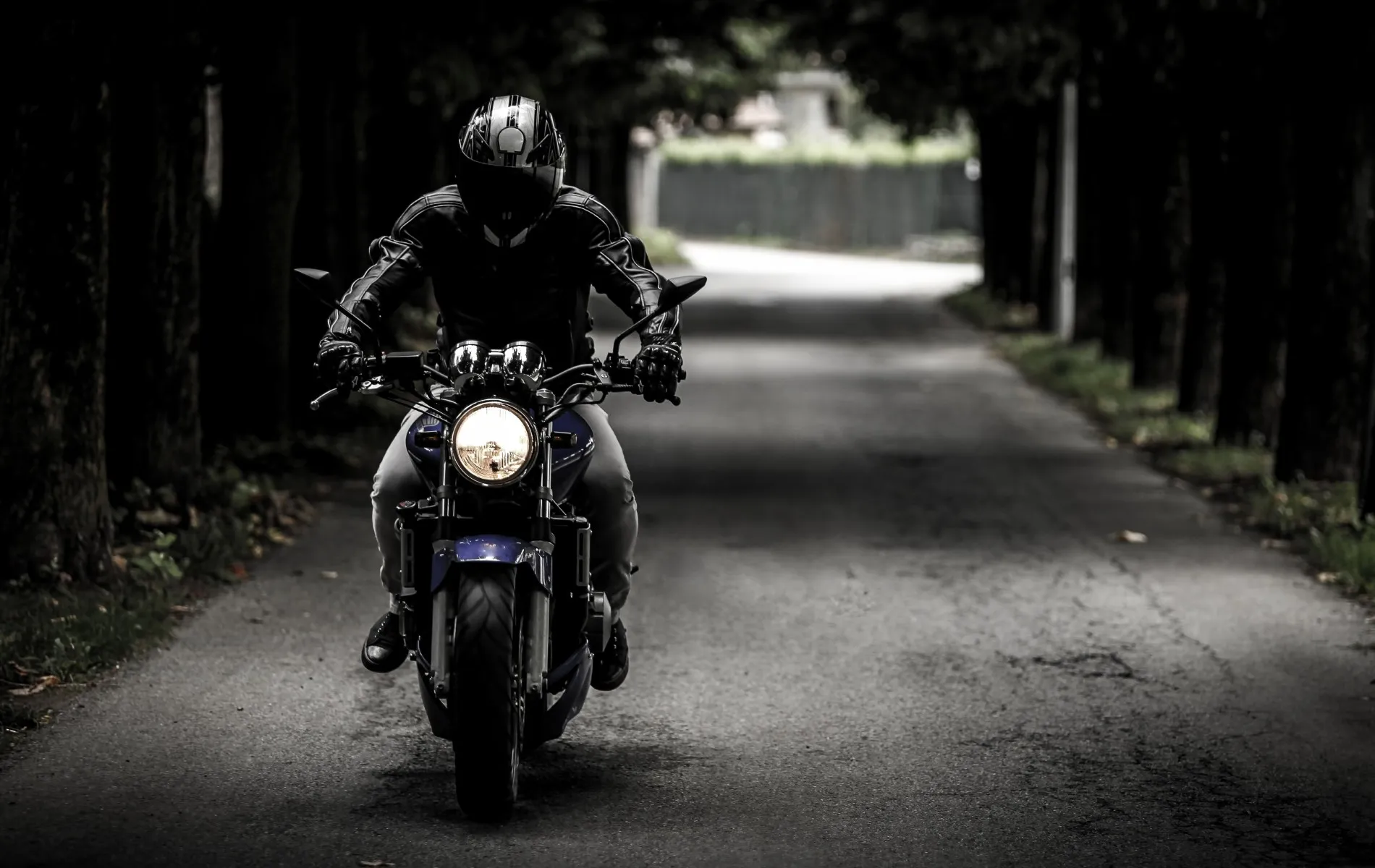 Imagem com um motociclista dirigindo numa rua vazia.