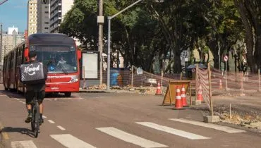 Imagem mostra um boqueio no trânsito de Curitiba, com um biarticulado e uma pessoa de bicicleta.