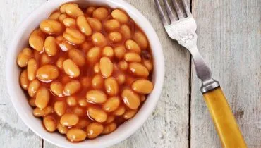 Imagem mostra uma cumbuca com feijão branco e um garfo ao lado.