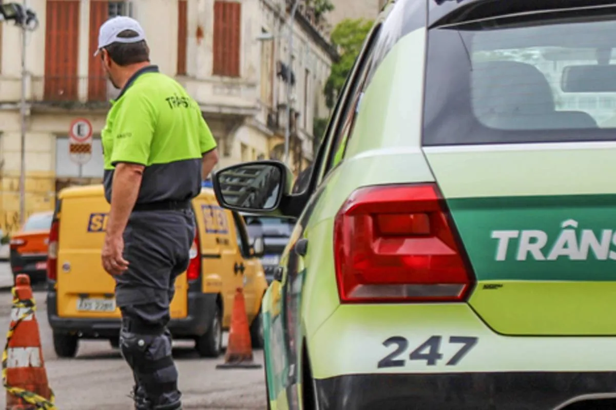 Imagem mostra uma viatura de trânsito com agentes e um carro dos correios ao fundo.