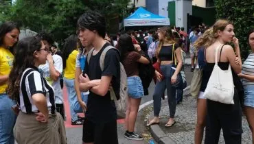 Imagem mostra estudantes em frente a uma escola.