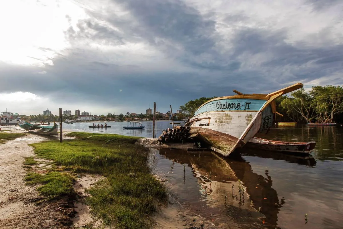 Imagem mostra uma parte da cidade de Paranaguá. com um barco e cidade ao fundo.