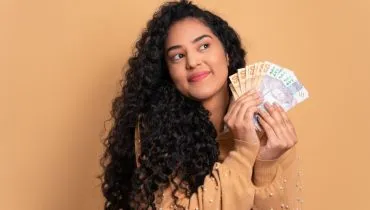 Imagem mostra uma mulher com um leque feito com notas de real em maos.
