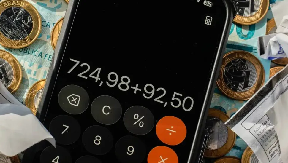 Imagem mostra uma calculadora com moedas e notas de real.