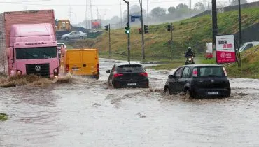 Imagem mostra veículos passando por uma área alagada em Curitiba.