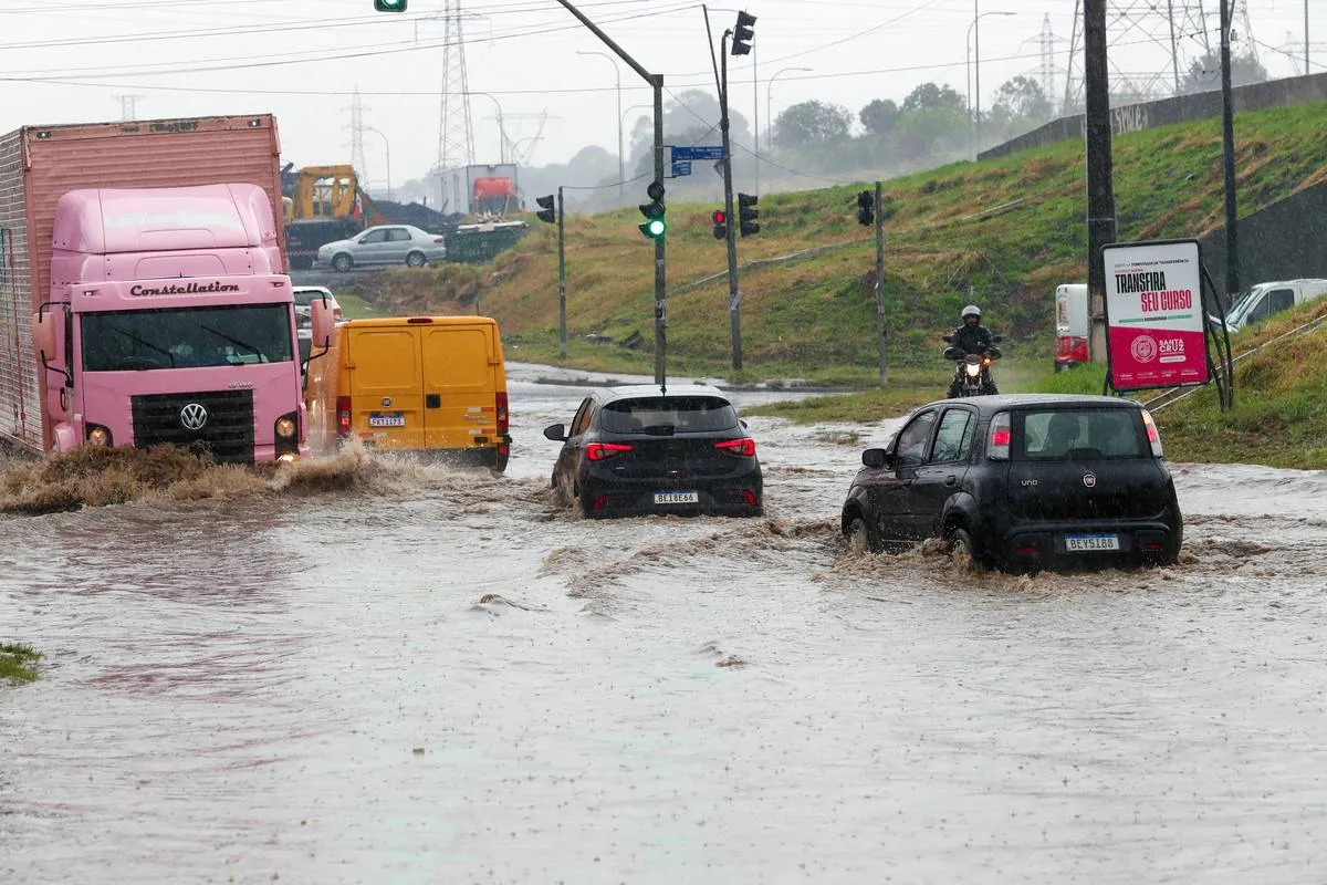 Imagem mostra veículos passando por uma área alagada em Curitiba.
