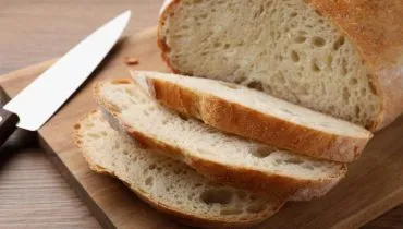 Imagem mostra um pão caseiro cortado em uma tábua de madeira com uma faca ao lado.
