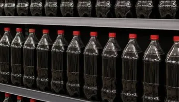 Imagem mostram garrafas de coca cola sem rótulos em uma prateleira de supermercado.