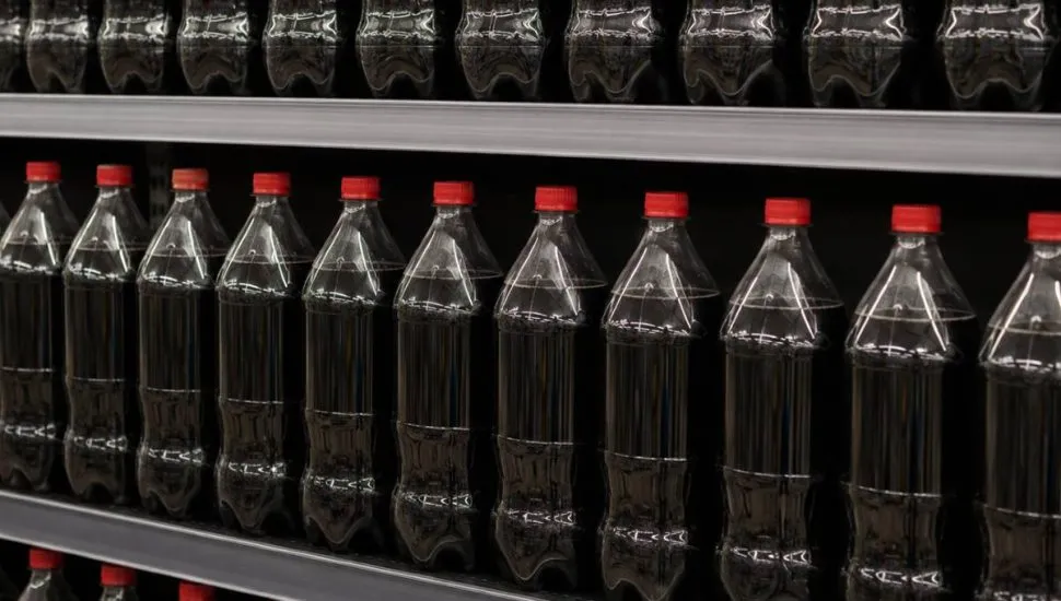 Imagem mostram garrafas de coca cola sem rótulos em uma prateleira de supermercado.