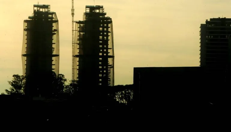 Imagem mostra dois prédios em construção num horizonte de fim de tarde no contra luz.
