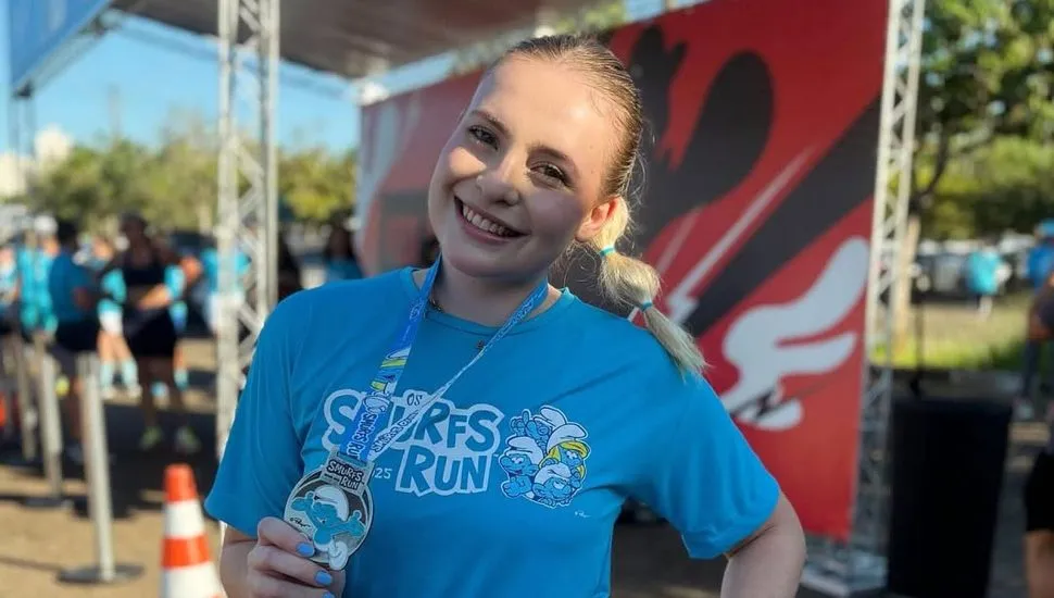imagem mostra jovem Ana Beatriz de roupa de corrida de rua, mostrando uma medalha conquistada em uma das provas