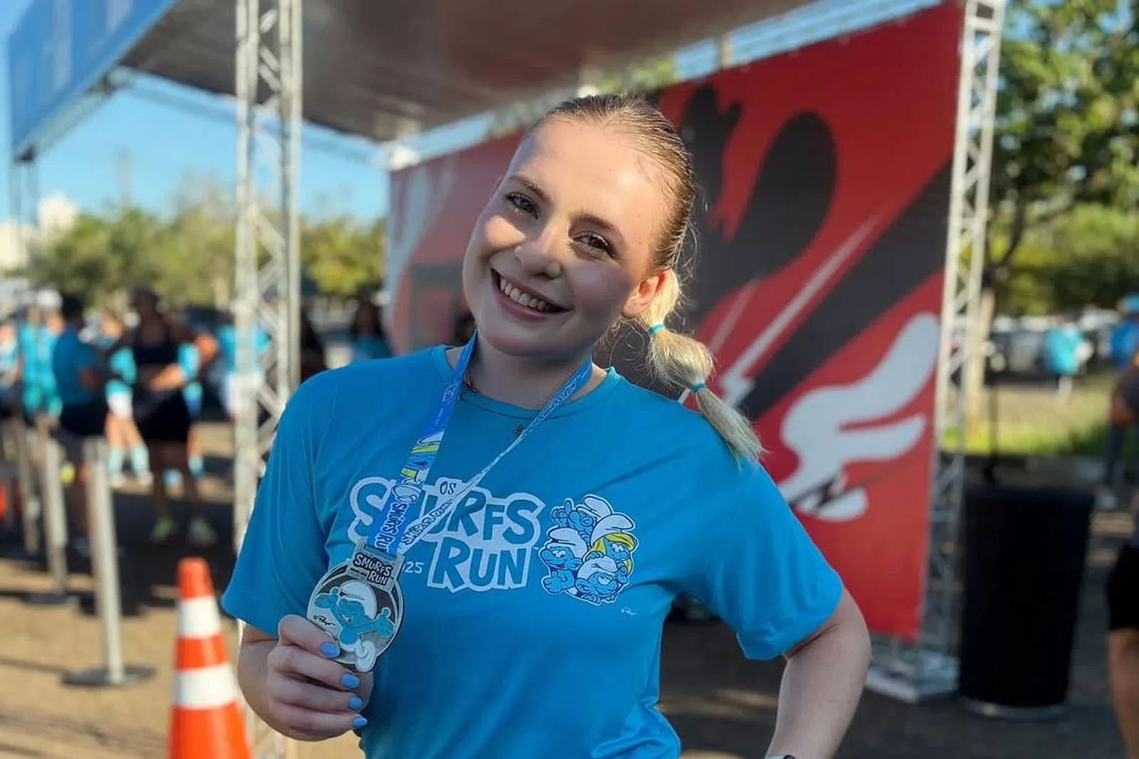 imagem mostra jovem Ana Beatriz de roupa de corrida de rua, mostrando uma medalha conquistada em uma das provas