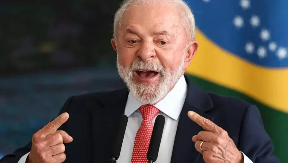 Imagem mostra Lula com a bandeira do Brasil ao fundo.