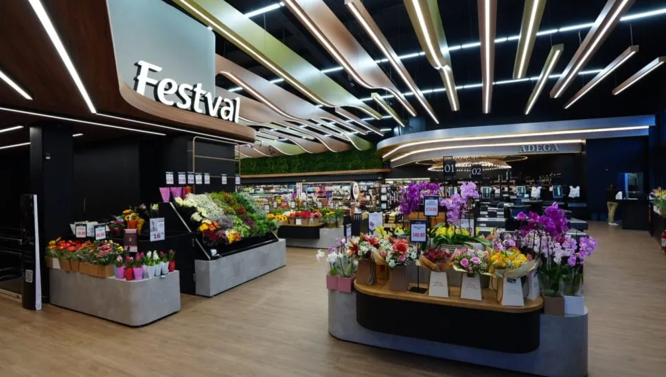 Imagem mostra o hall de entrada do supermercado, com um balcão chio de flores em primeiro plano e demais setores ao fundo