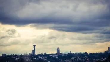 Imagem mostra o céu carregado em Curitiba, com prédios ao fundo e nuvens pesadas.
