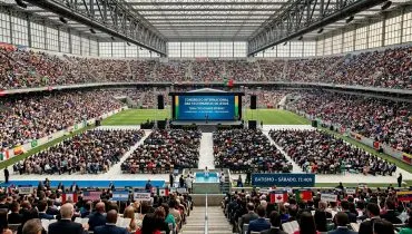 Imagem mostra um estádio lotado, com palco no centro e cadeiras espalhadas pelo gramado com participantes do congresso