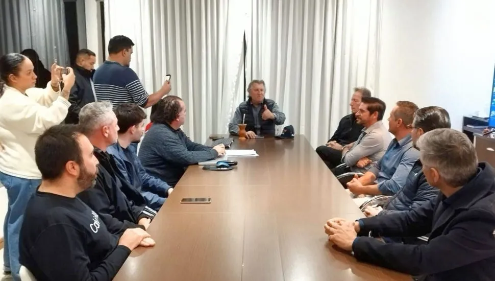 vários homens reunidos ao redor de uma mesa, com um deles na ponta, comandando uma reunião