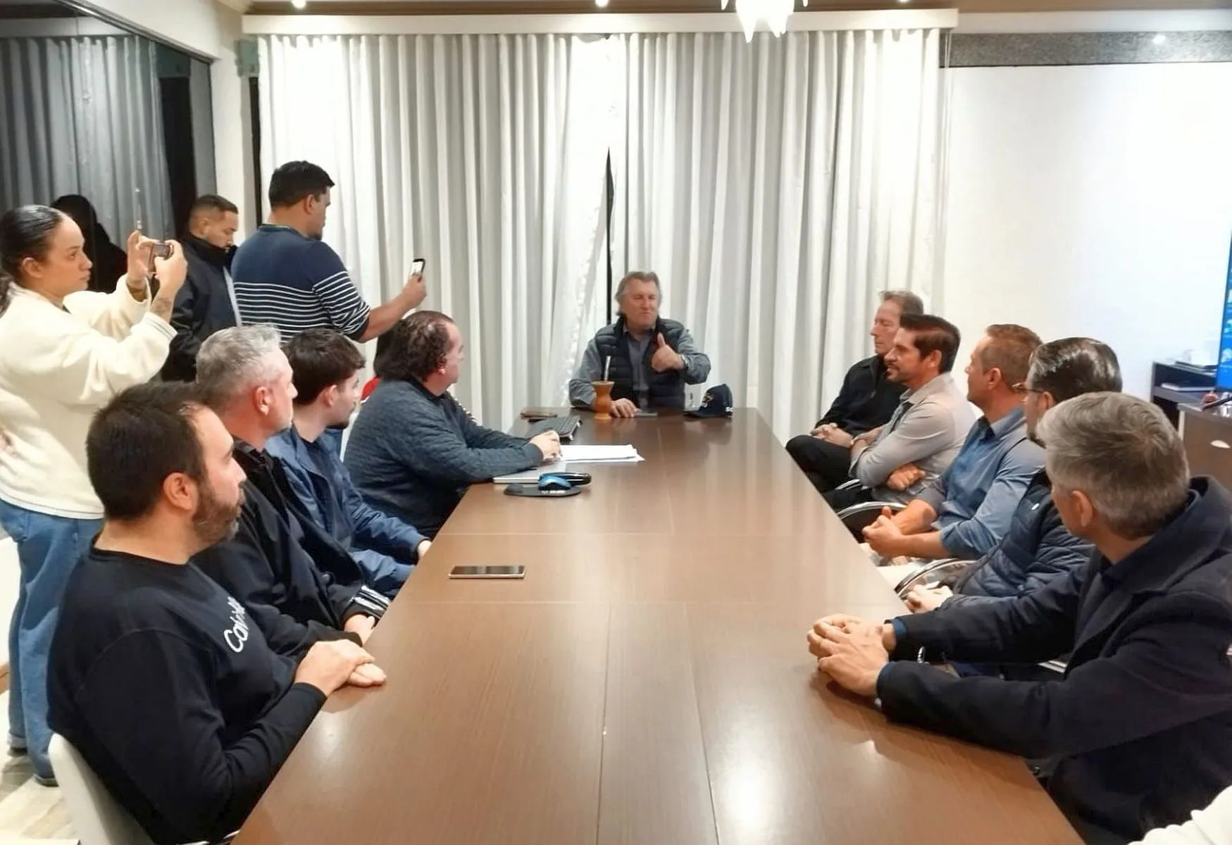 vários homens reunidos ao redor de uma mesa, com um deles na ponta, comandando uma reunião