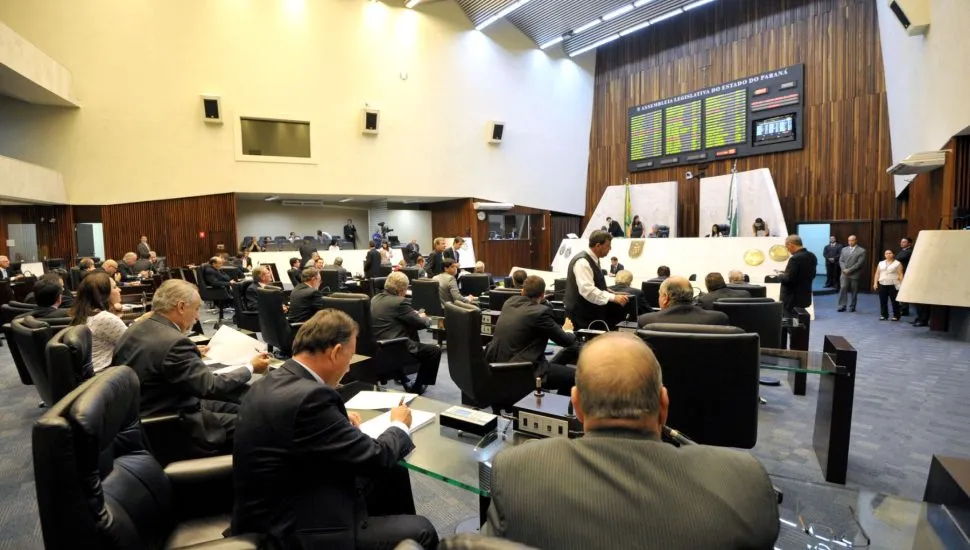 Imagem mostra plenário da Assembleia Legislativa do Paraná vista da posição dos deputados, com painel de votação e mesa diretora ao fundo