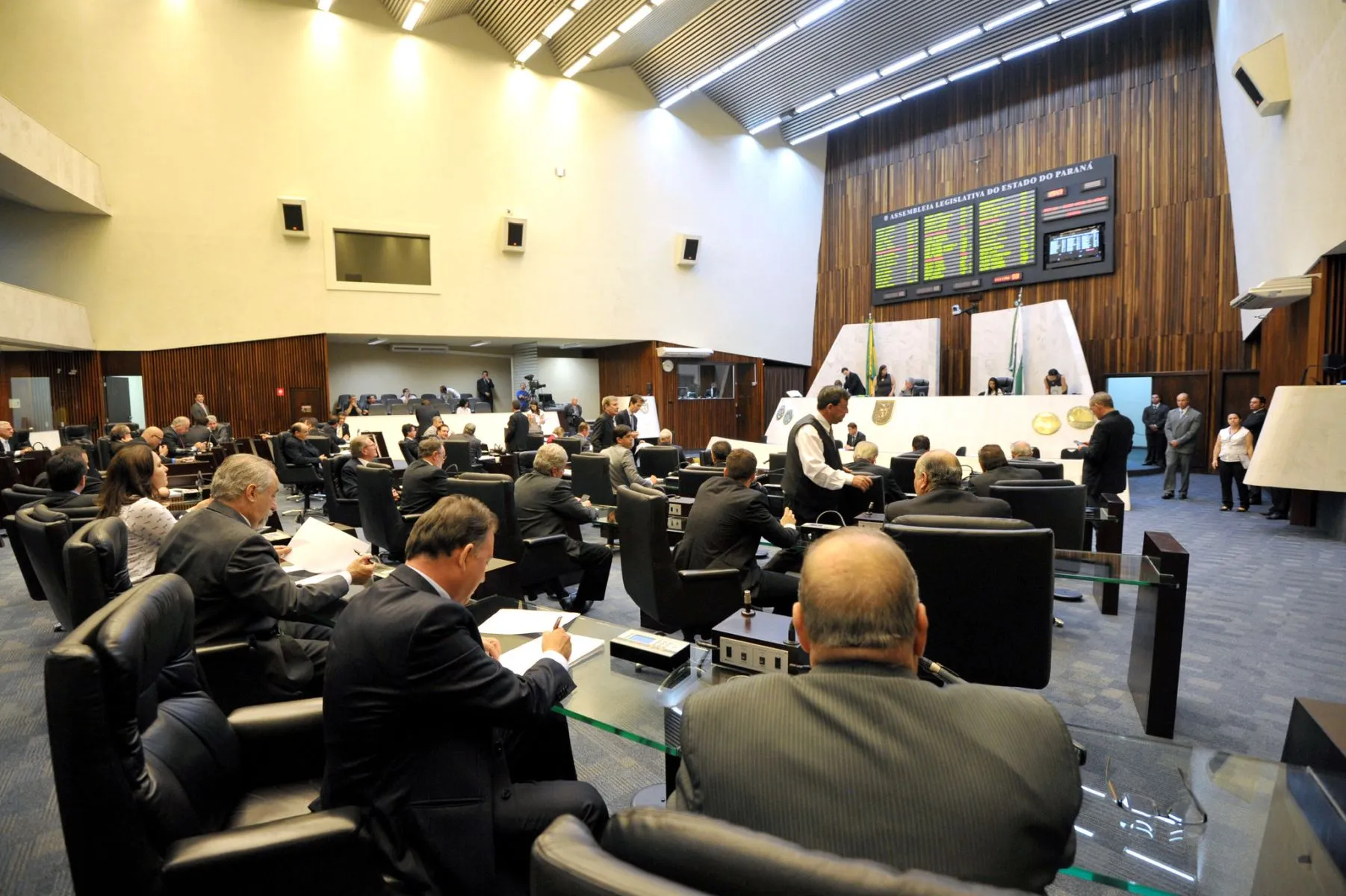 Imagem mostra plenário da Assembleia Legislativa do Paraná vista da posição dos deputados, com painel de votação e mesa diretora ao fundo