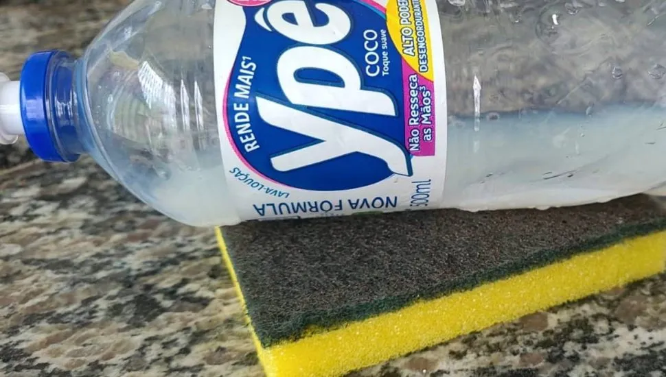Imagem mostra um frasco plástico de detergente líquido Ypê Coco deitado sobre uma esponja de lavar louça amarela e verde.