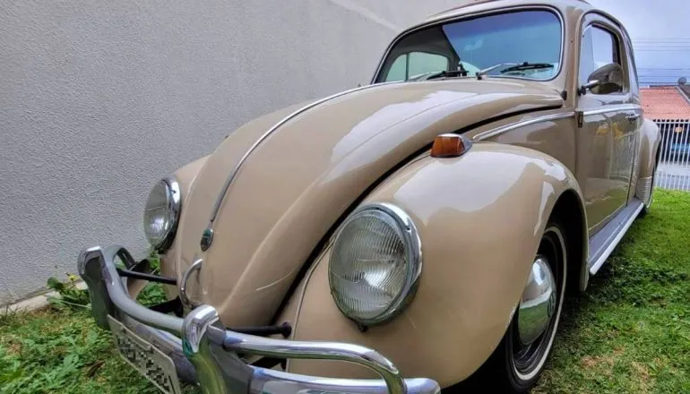 Imagem mostra um fusca bege 1969 em um gramado.