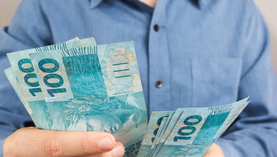 Imagem mostra uma pessoa contando notas de R$ 100.