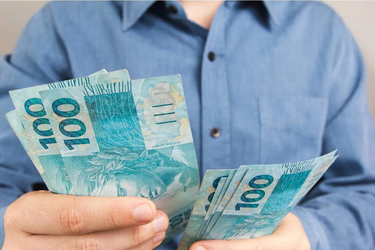 Imagem mostra uma pessoa contando notas de R$ 100.