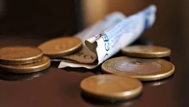 Imagem mostra moedas e uma nota de R$ 2 em cima de uma mesa.
