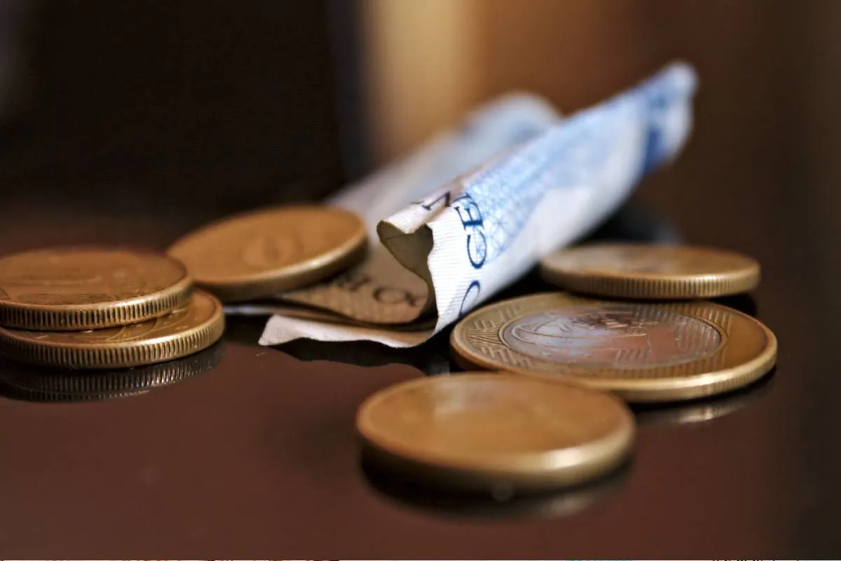 Imagem mostra moedas e uma nota de R$ 2 em cima de uma mesa.