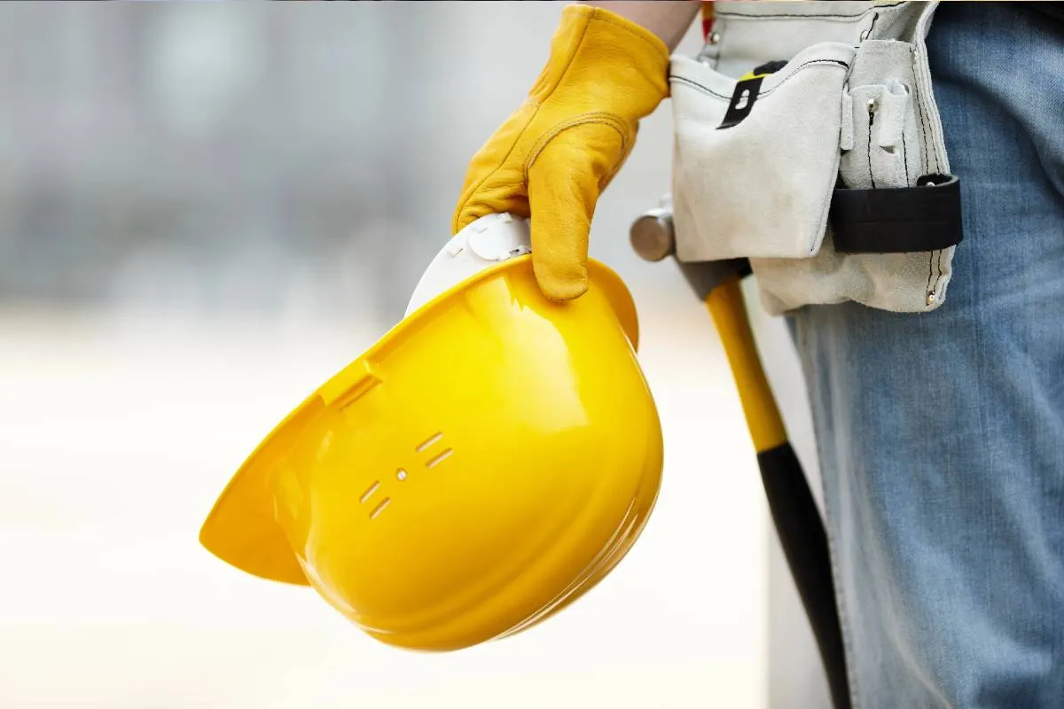 Imagem mostra um homem em uma obra carregando um capacete, um EPI de construção.