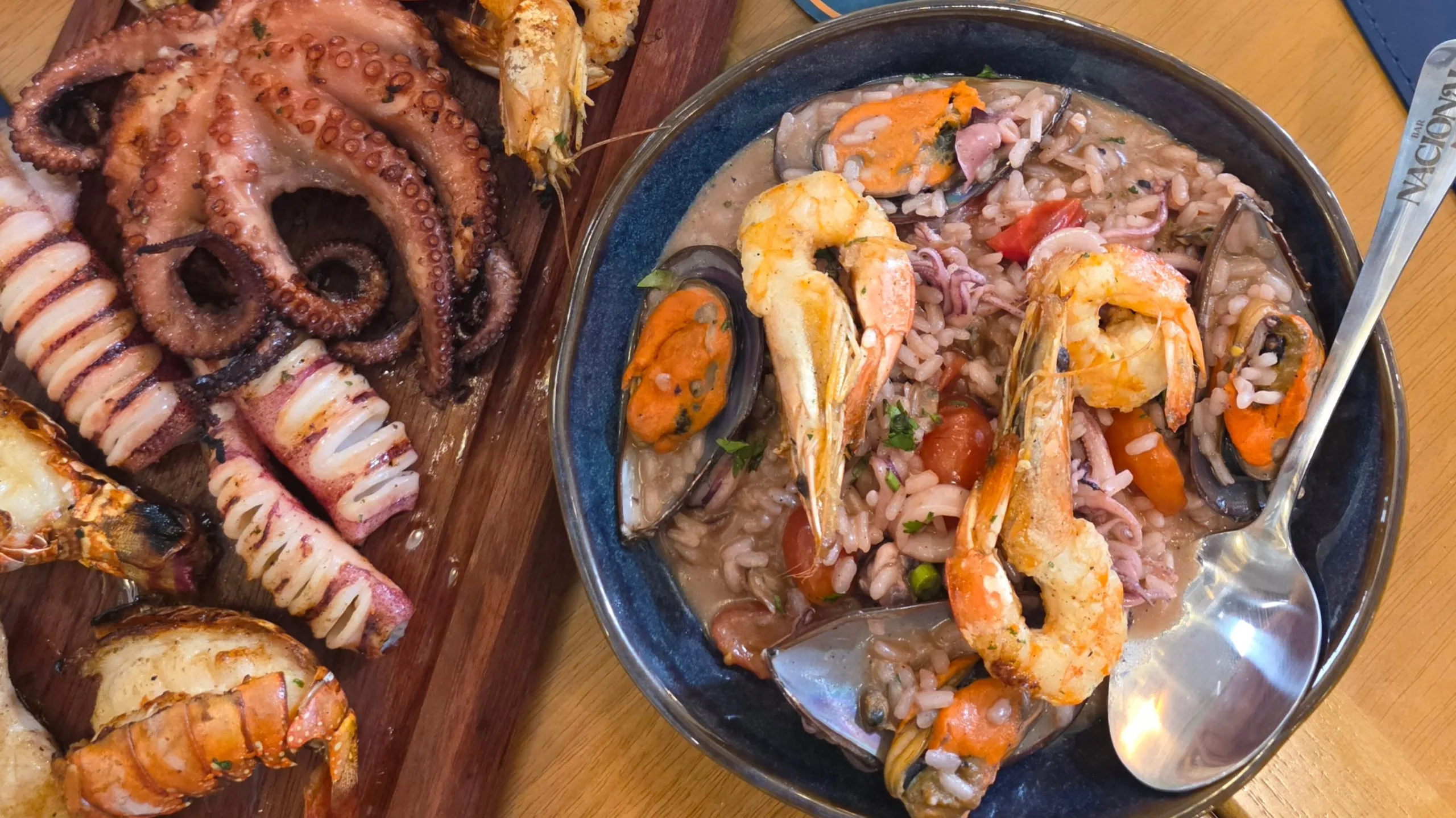 Parrilhada com camarões em panela e tábua com polvo e outros frutos do mar ao lado.